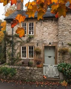 an old stone house with autumn leaves on the ground