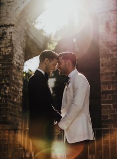 two men standing next to each other in front of a brick building with sunlight coming through the windows