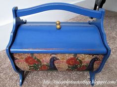 a blue painted wooden toy chest with flowers and birds on the front, sitting on carpeted floor