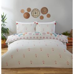 a white bed topped with lots of pillows next to a wall mounted clock and potted plants