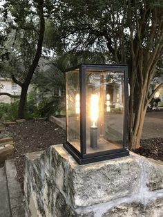 an old fashioned lantern is sitting on top of a stone block in front of a tree