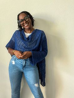 a woman standing in front of a white wall wearing ripped jeans and a blue sweater