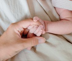 a person holding a baby's hand while laying on top of a white sheet