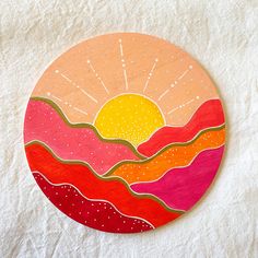 a painted wooden circle with mountains and sun in the background on a white surface,