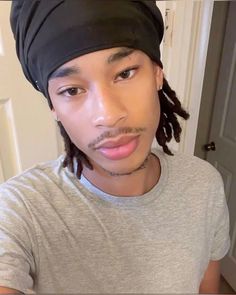 a man with dreadlocks and a beanie looks at the camera while wearing a gray shirt