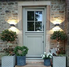 two planters with flowers in front of a white door and some lights on the outside