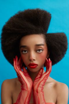 a woman with an afro is holding her hands to her face and wearing red gloves