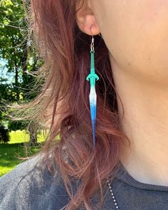 a close up of a person wearing earrings with blue and green feathers hanging from them