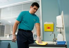 a man in a blue shirt is cleaning a kitchen sink with a yellow sponge on it