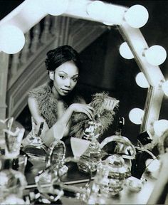 a black and white photo of a woman sitting in front of a mirror with lights