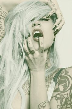 a woman with white hair and tattoos holding her hands to her face