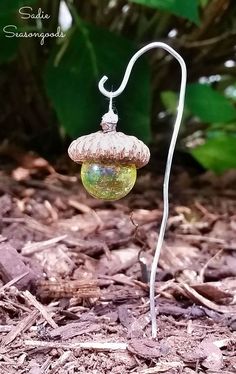 a glass ornament hanging from a wire on the ground with leaves in the background