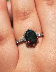 a close up of a person's hand holding an engagement ring with a green and red stone