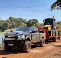 a large truck towing a tractor down a dirt road next to a body of water