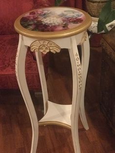 a small white table with flowers painted on the top and gold trimming around it