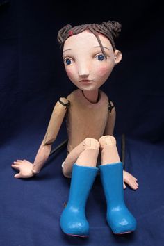 a wooden doll sitting on the ground wearing blue boots and holding a pair of scissors