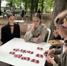 three women sitting at a table with cards in front of them and one woman holding a plate of food