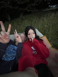 two people laying in the grass making peace signs with their hands while sitting next to each other