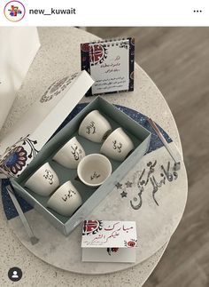 an open box with six white cups on top of a table next to some cards