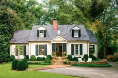 a white house with black shutters and green grass in the front yard, surrounded by trees