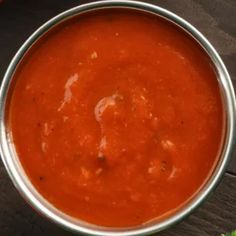 a metal bowl filled with red sauce on top of a wooden table