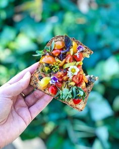 a person holding up a piece of bread with various vegetables on it