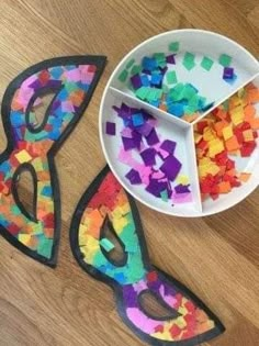 two masks and a bowl of colored confetti on a wooden table with scissors