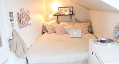 a small bedroom with a laptop on the bed and lots of pillows in it's corner