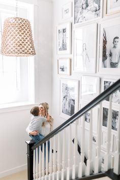 a man and woman kissing on the stairs in front of many framed pictures, with a lamp hanging above them