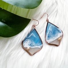 a pair of blue and white earrings sitting on top of a furnishing next to a plant