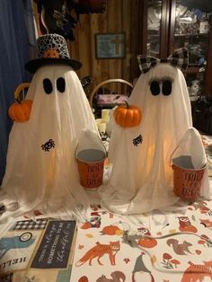 two plastic ghost buckets sitting on top of a table covered in white cloth and orange pumpkins