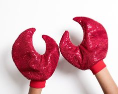 pair of red sequined gloves held up by two hands, on white background