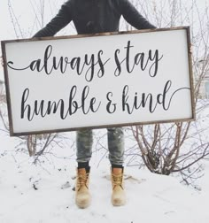 a person standing in the snow holding a sign that says, always stay humble and kind