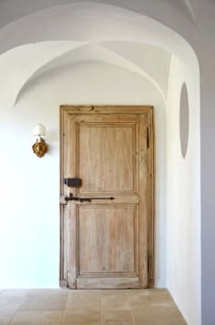 an old wooden door is in the corner of a white room with arched doorways