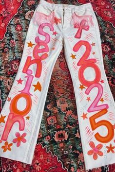 two white pants with pink and orange letters on them sitting on top of a rug