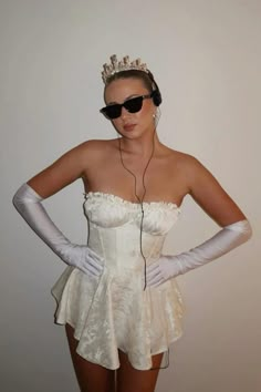 a woman wearing white gloves and a tiara with headphones on her ears is standing in front of a wall