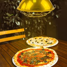 two pizzas sitting on top of white plates next to a yellow hanging light fixture