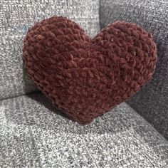 a heart shaped pillow sitting on the back of a gray couch with grey flannel upholster