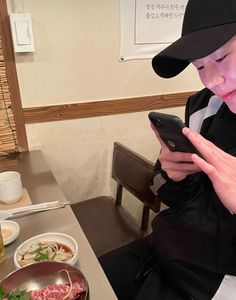 a person sitting at a table with food and a cell phone in their hand while looking at the screen