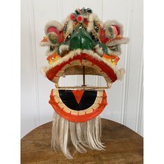 an elaborate chinese mask is displayed on a wooden table in front of a white wall