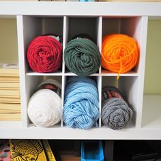 several skeins of yarn are sitting in a white storage unit on the floor