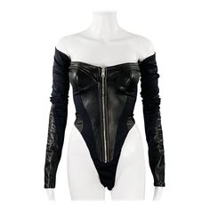 MUGLER bodysuit in a black lambskin leather and stretchy nylon blend featuring an off-shoulder style, paneled construction, silver tone metal zipper front, and a three snap crotch closure. Made in Poland.Excellent Pre-Owned Condition. Marked: 34 Measurements: Bust: 30 inches Sleeve: 24.5 inches Length: 21 inches Sui Generis Reference: 133581 Category: Overalls & Jumpsuits More Details Brand: MUGLER Gender: Female Size: 2 Color: Black Fabric: Nylon Blend Pattern: Mixed Materials Type of Leather: Mugler Bodysuit, Leather Leotard, Latex Jumpsuit, Overalls Black, Leather Bodysuit, Vintage Overalls, Leotard Bodysuit, Slim Aarons, Silver Fabric