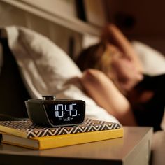 a woman laying in bed next to a book and alarm clock