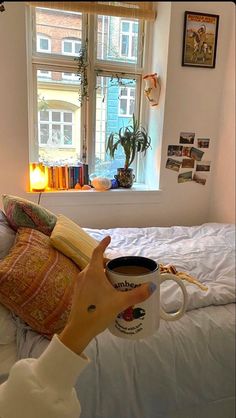 a person holding a coffee mug in front of a window with books on the windowsill