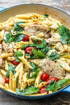 a skillet filled with pasta, meat and spinach on top of a wooden table