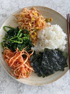 a white plate topped with rice and veggies next to two chopsticks