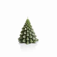 a small green christmas tree sitting on top of a white table next to a candle