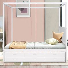 a white bed with drawers underneath it in front of a pink wall and wooden floor