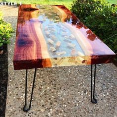 a wooden table sitting on top of a gravel ground next to bushes and trees in the background