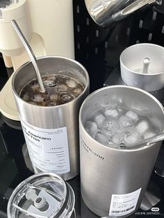 two buckets filled with ice and water sitting on top of a counter next to cups